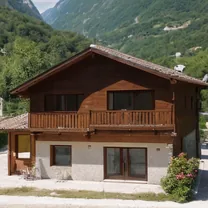 A wooden chalet beside a turquoise river with mountains rising behind it